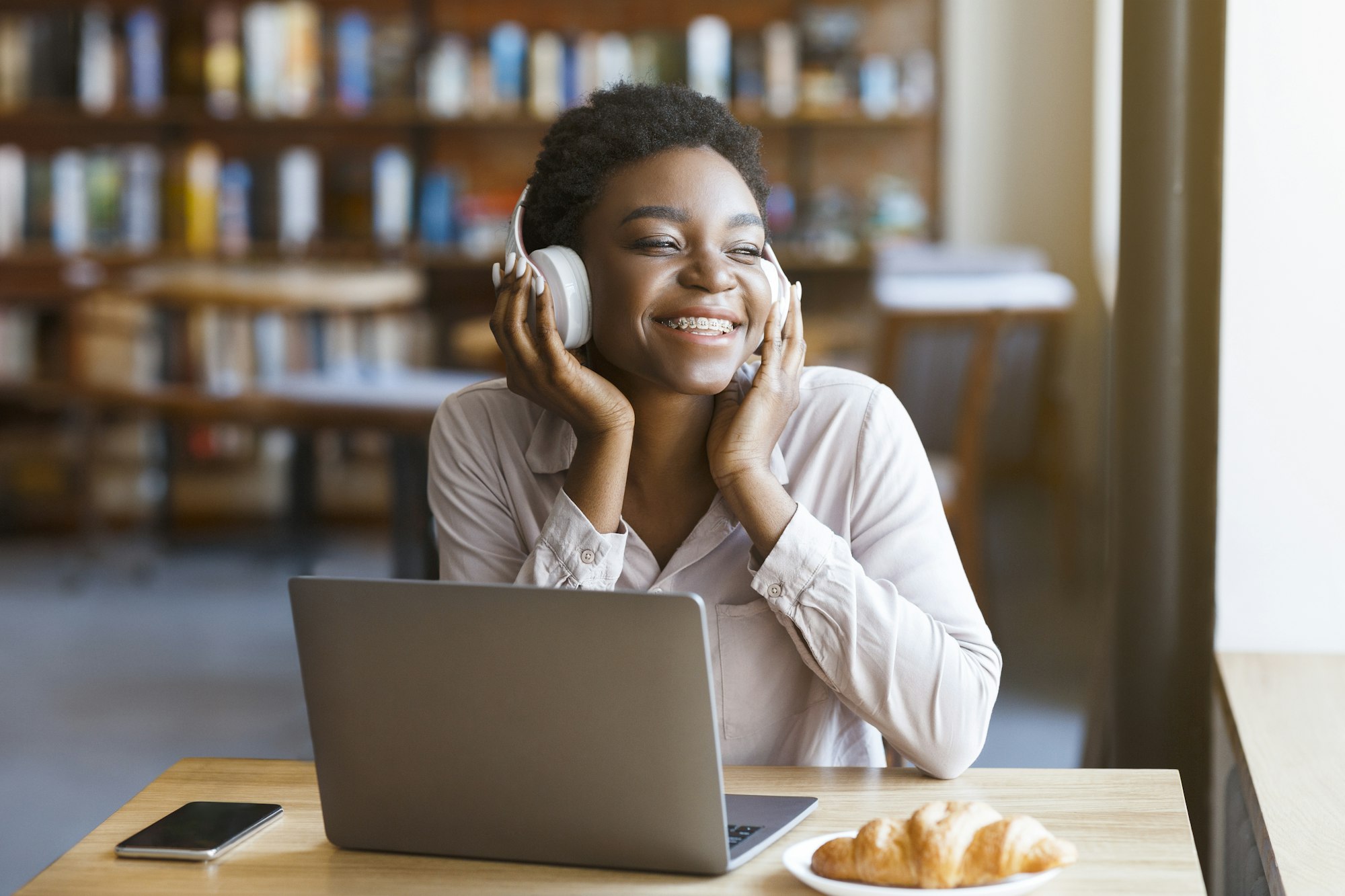 Black woman listening to music with headset, laptop in cafe