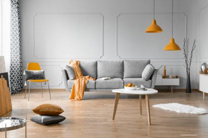 Fashionable living room interior design with grey couch, wooden coffee table and orange accents