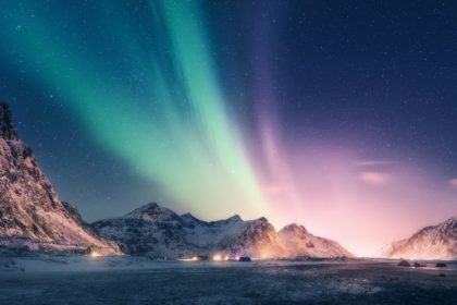 Green and purple aurora borealis over snowy mountains