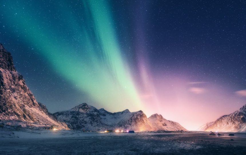 Green and purple aurora borealis over snowy mountains